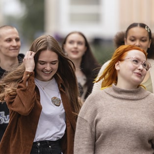 Viisi nuorta kävelee hymyillen kadulla.