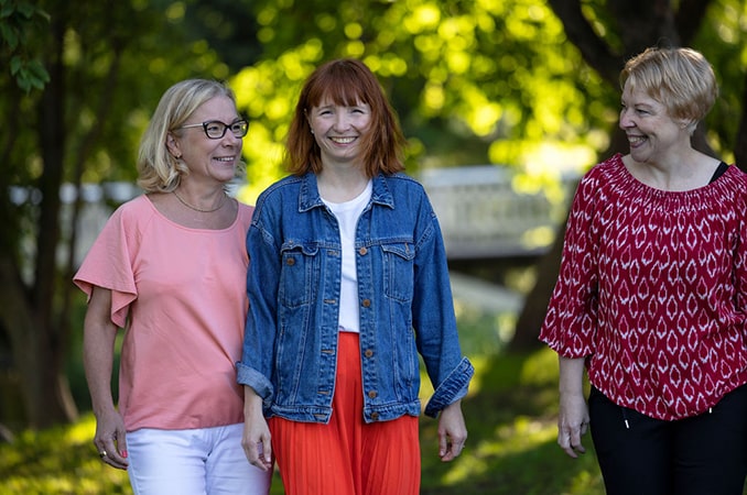 Kolme naista kävelee puistossa hymyssä suin.