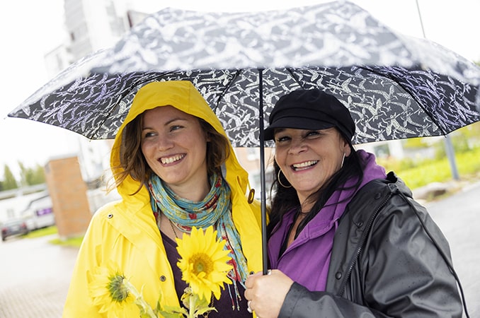 Kaksi naista hymyilee sateenvarjon alla.