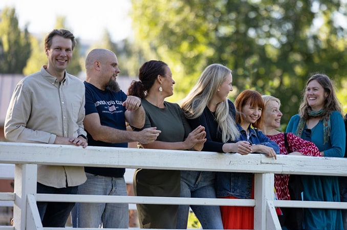 Useita ihmisiä seisoo sillalla ja kaikki hymyilevät ja katsovat toisiaan.