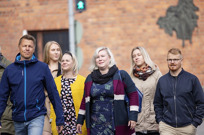 Neljä naista ja kaksi miestä kävelevät kadulla.