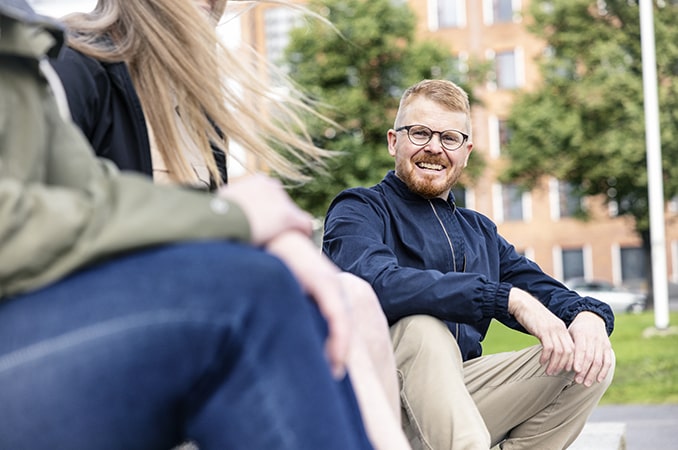 Mies istuu ulkona ja hymyilee kameralle.