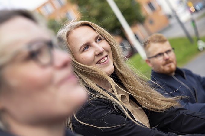 Kaksi aikuista istuu nuoren kanssa portailla. Nuori hymyilee.